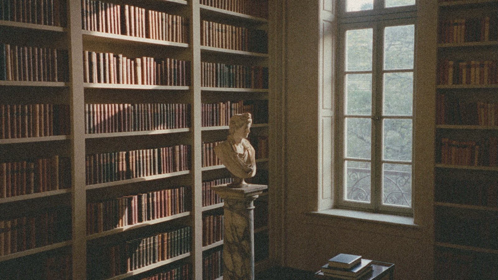 Sunlit private library with tall bookshelves and a marble bust near an arched window